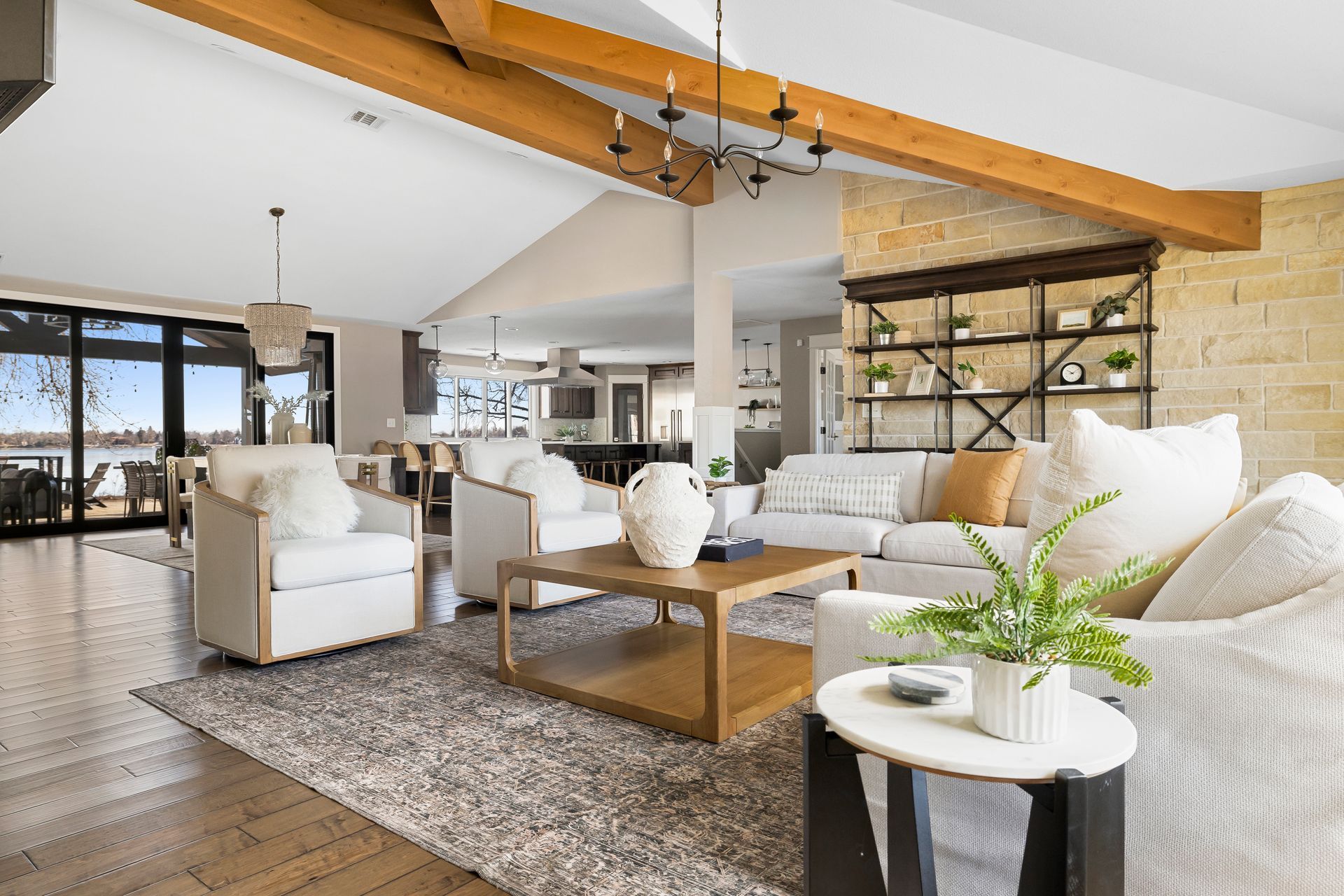 Living room with white furniture, wooden beams, stone wall, and view of water.