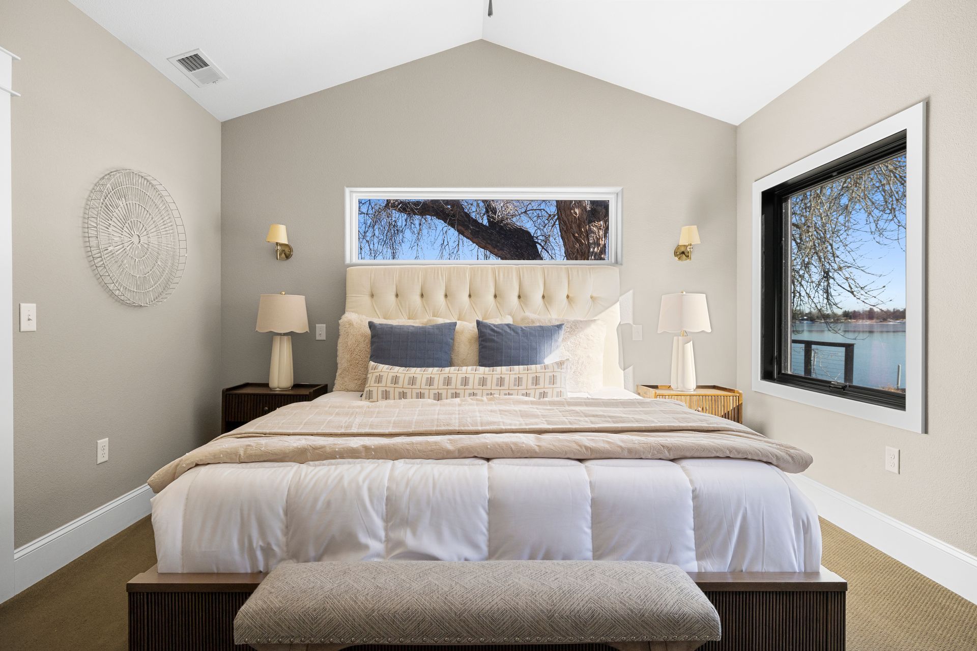 Bedroom with a large bed, tufted headboard, and two windows. Neutral color palette with natural light.