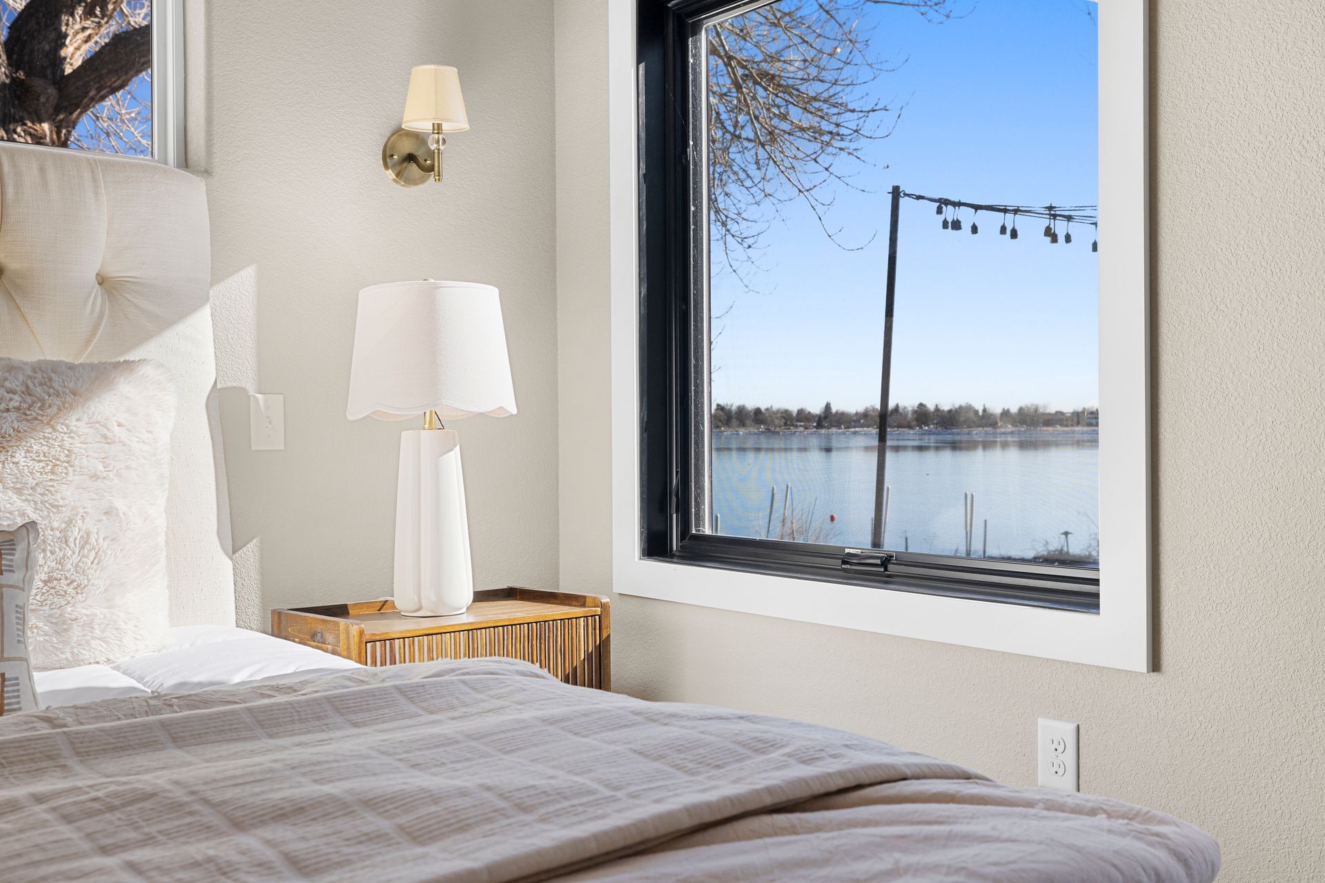 Bedroom with bed, bedside table, lamp, and window with a lake view.