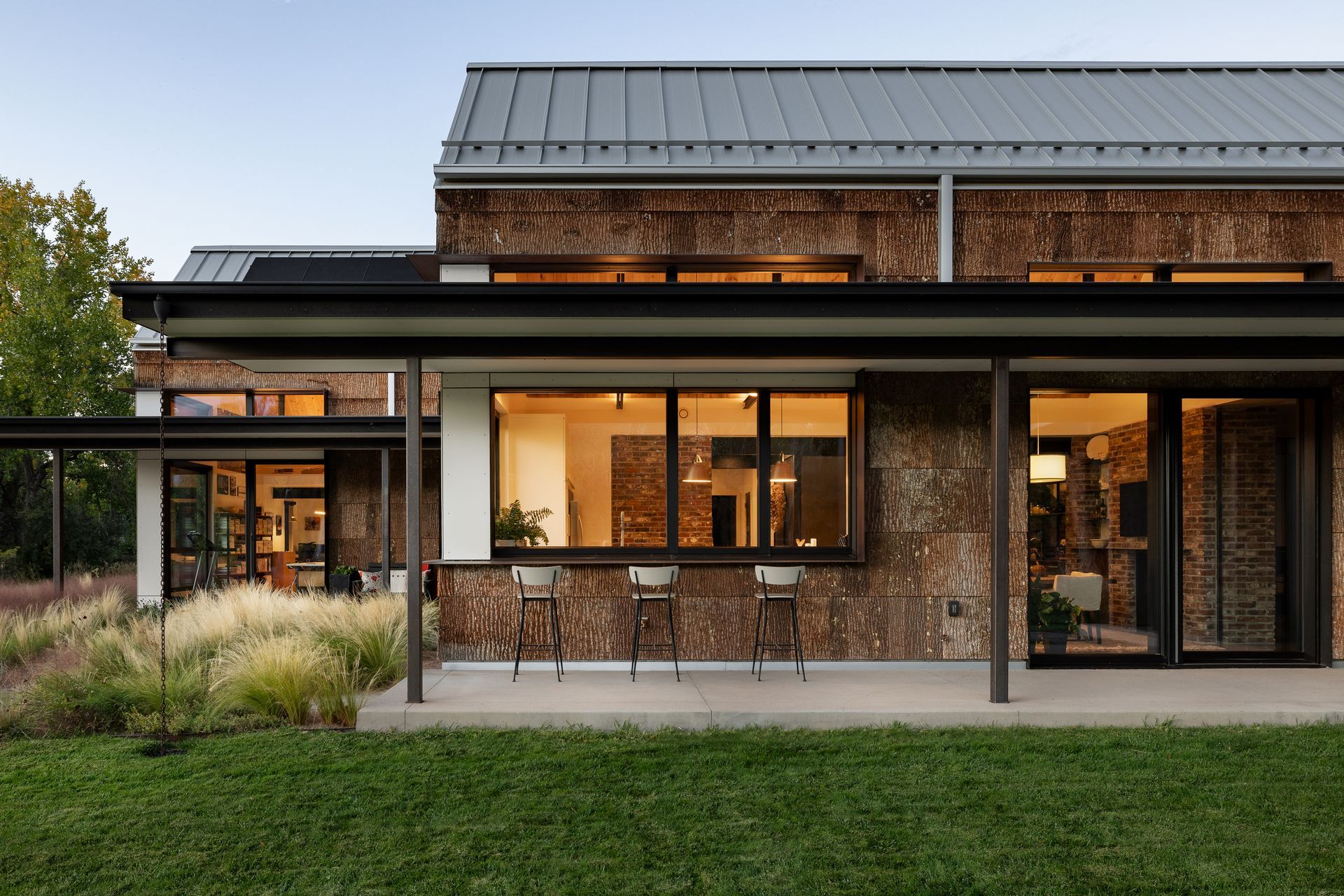 Modern home exterior with textured facade, large windows, and outdoor seating area.
