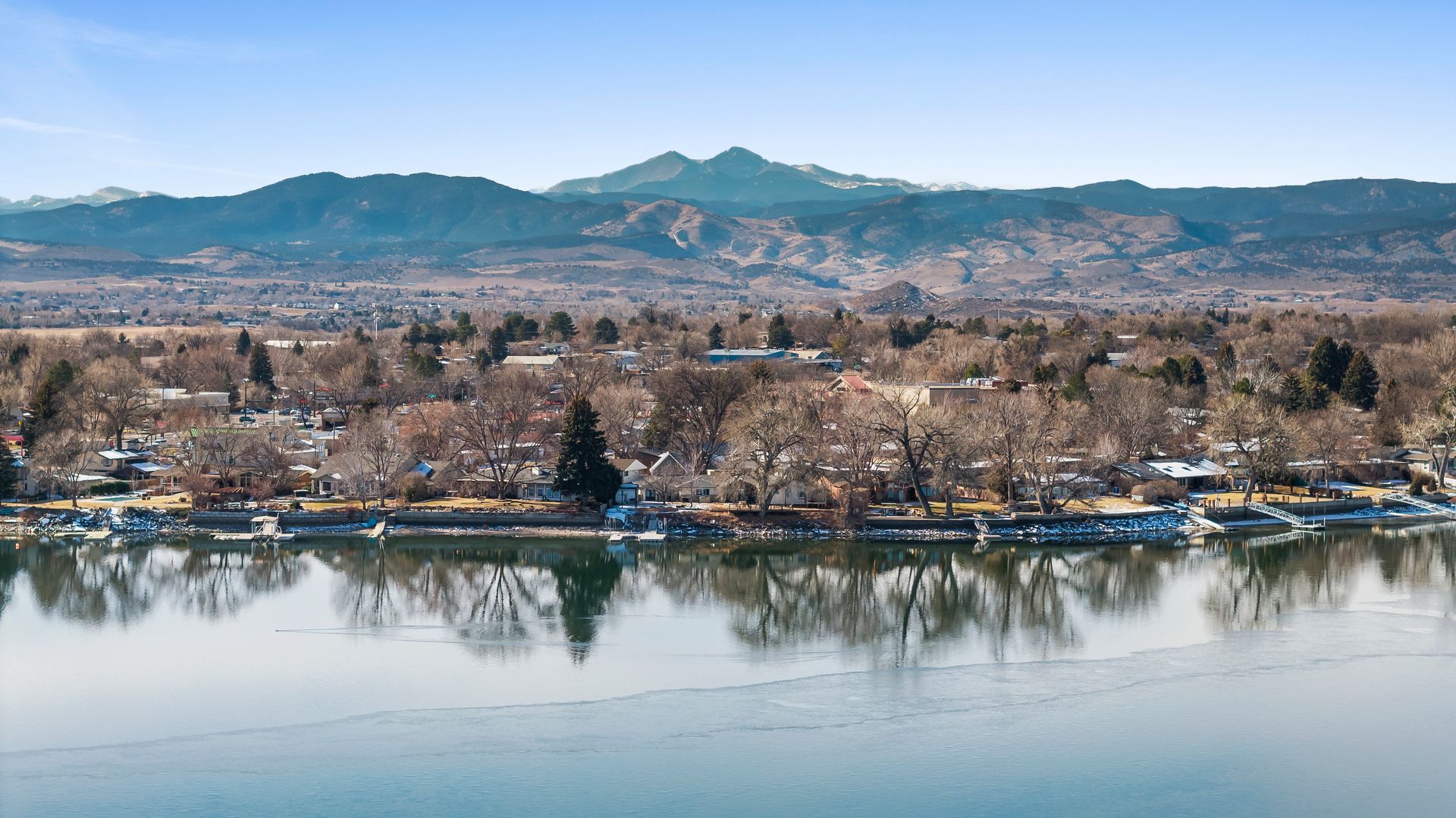 View of a lake with leafless trees and a mountain range in the background.