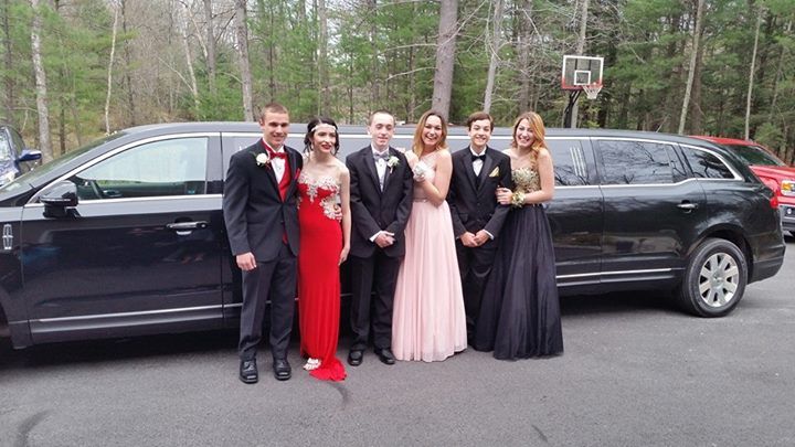 Group of teens in formal wear by a black limousine.