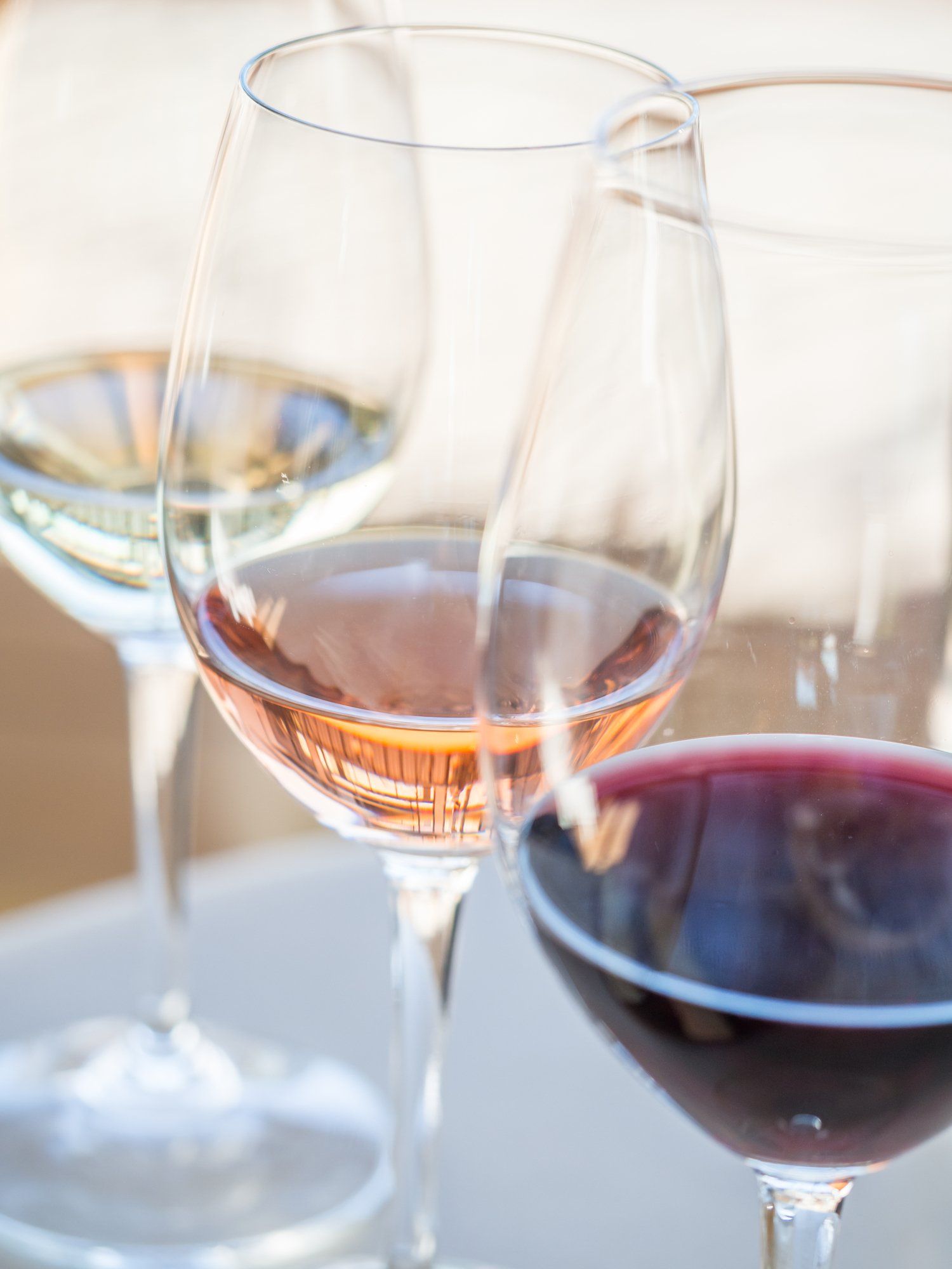 Wine glasses with white, rosé, and red wine, arranged on a light background.