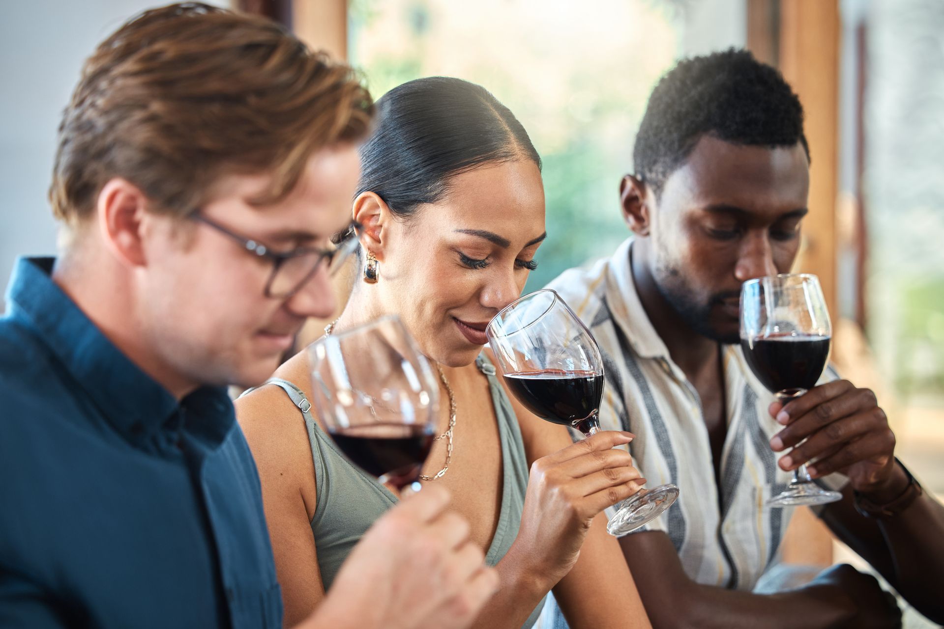 A diverse group of three people, two men and one woman, taste wine with a cup each.