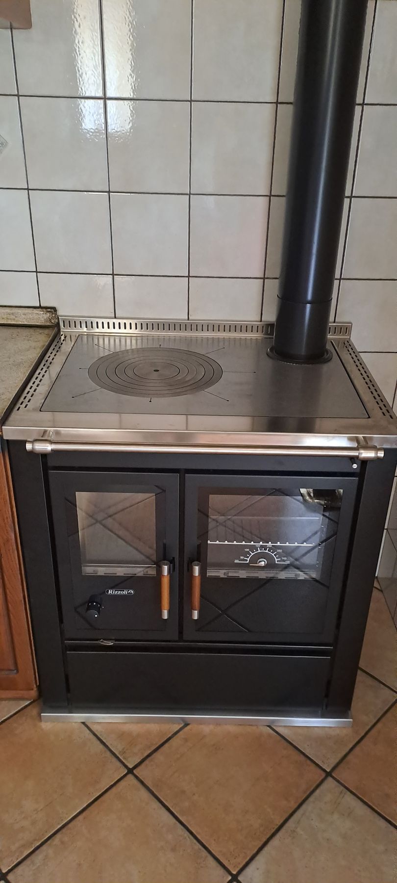 Stufa a legna nera con sportelli in vetro, piano in acciaio inossidabile e camino in cucina.