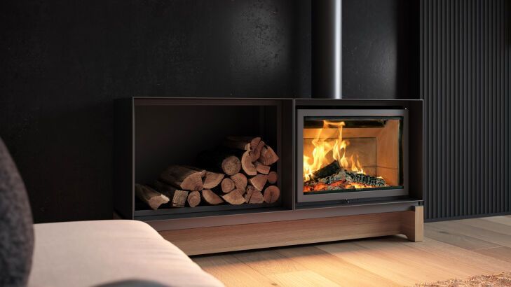 Camino con fiamme ardenti accanto a un vano porta-legna. Ambiente scuro, toni neutri.