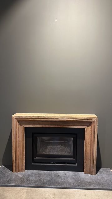 Camino con mensola in legno e interno nero contro una parete grigia.