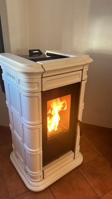 Una stufa a pellet bianca con il fuoco acceso all'interno, posizionata su un pavimento piastrellato.