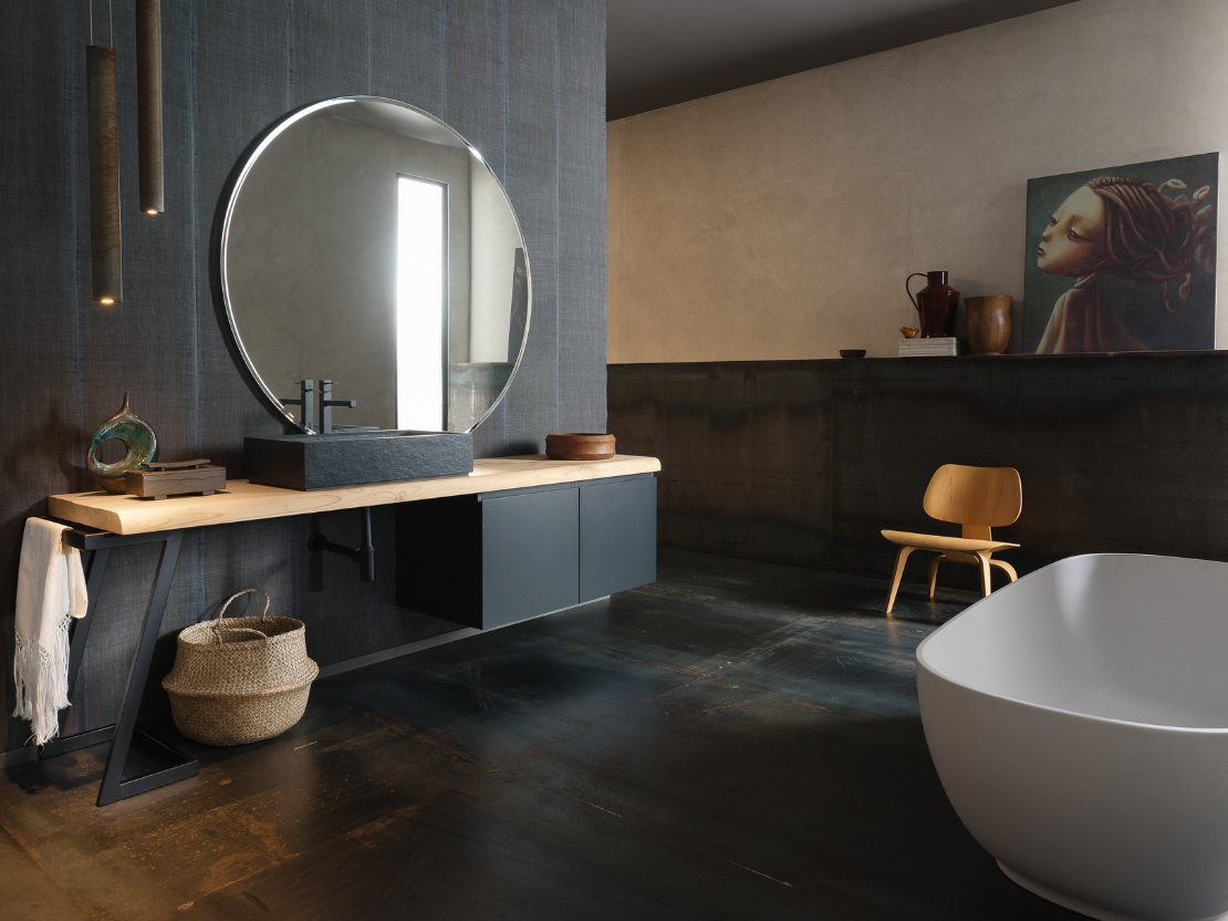 Bagno moderno con specchio rotondo, piano di lavoro in legno, mobili scuri e vasca da bagno indipendente.