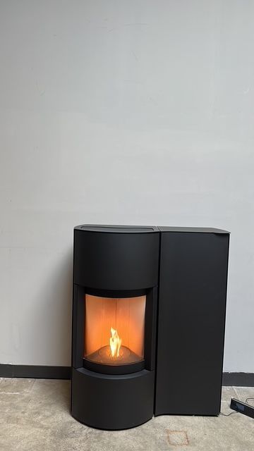 Stufa a pellet nera con fiamme contro una parete bianca.