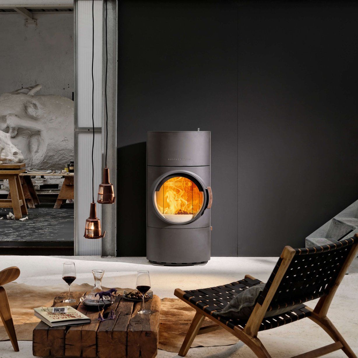 Una moderna stufa a legna grigia in un soggiorno minimalista, con fiamme visibili.