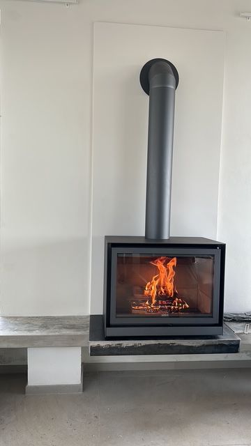 Camino con fiamme ardenti, canna fumaria grigia, su una superficie grigia e bianca.