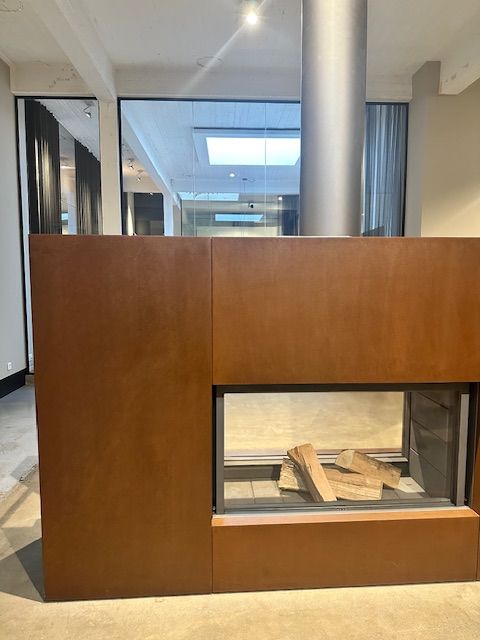 Caminetto moderno con pannelli in metallo arrugginito, rivestimento in vetro e ceppi di legna all'interno.