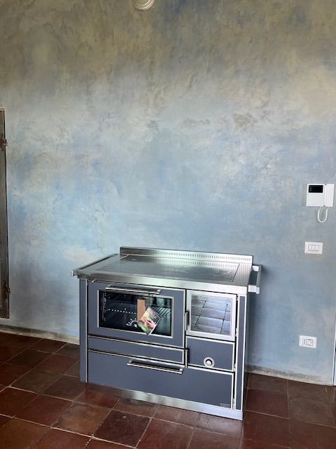 Stufa grigia e argento contro una parete blu screziata. Pavimento piastrellato marrone.