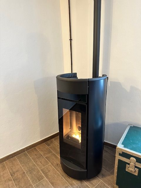 Stufa a pellet nera con frontale in vetro, in un angolo accanto a una scatola di legno.