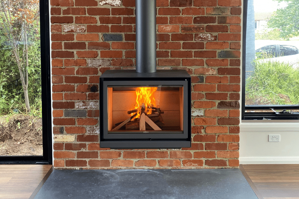 Camino con ceppi ardenti incastonati nel muro di mattoni, con camino, finestre e pavimento in legno.