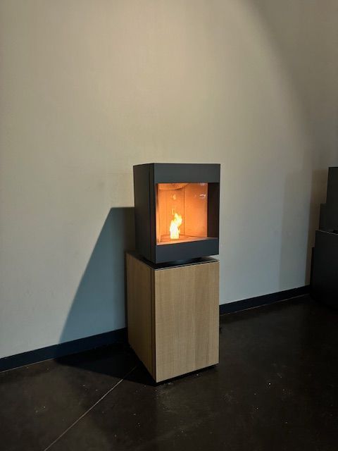 Caminetto moderno con fiamma accesa su un ceppo di legno, contro una parete grigia.