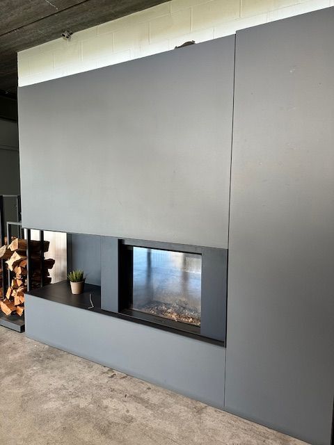 Moderno camino grigio incassato in una parete, con fuoco acceso e una piccola pianta sulla mensola.