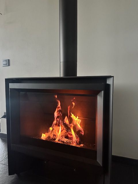 Caminetto con fiamme, struttura in metallo nero, canna fumaria nera, ambiente interno.