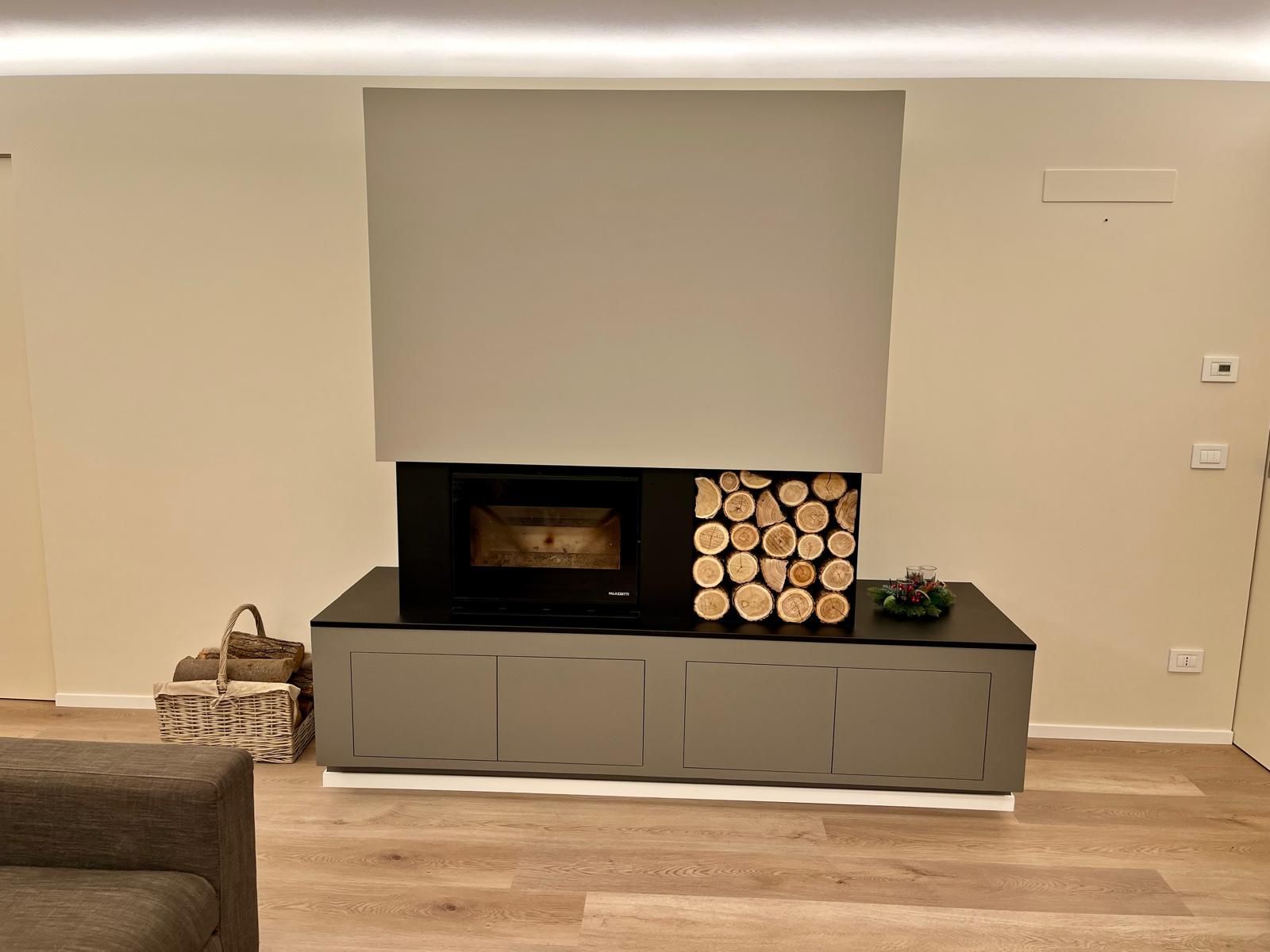 Camino con legnaia, mobili grigi e una parete dai toni neutri in un soggiorno.