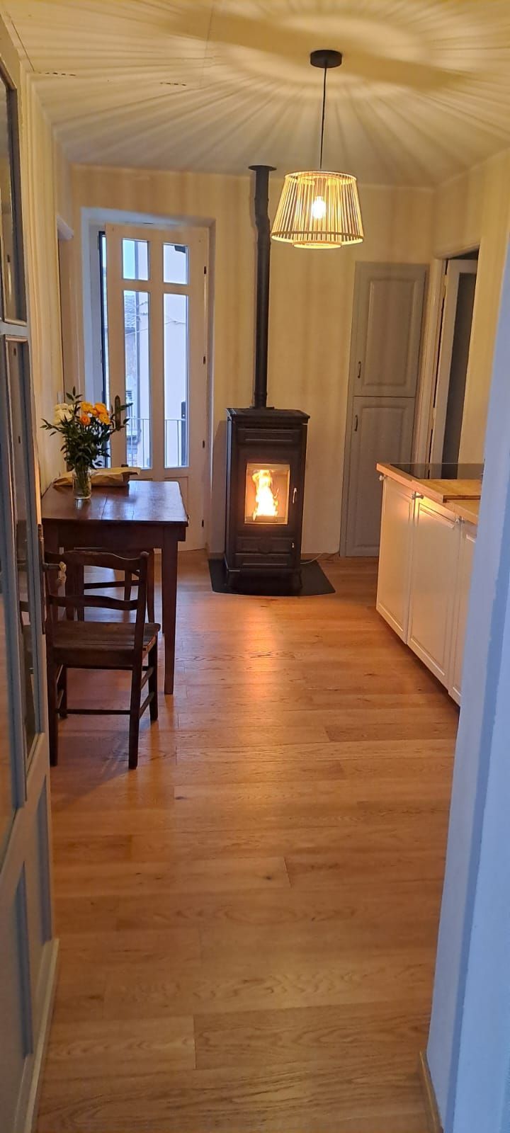 Interni accoglienti con stufa a legna accesa, pavimento in legno, tavolo da pranzo con fiori e lampadario decorativo.
