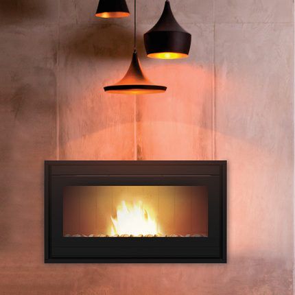 Camino con fiamme, sotto tre lampade sospese, contro una parete strutturata.