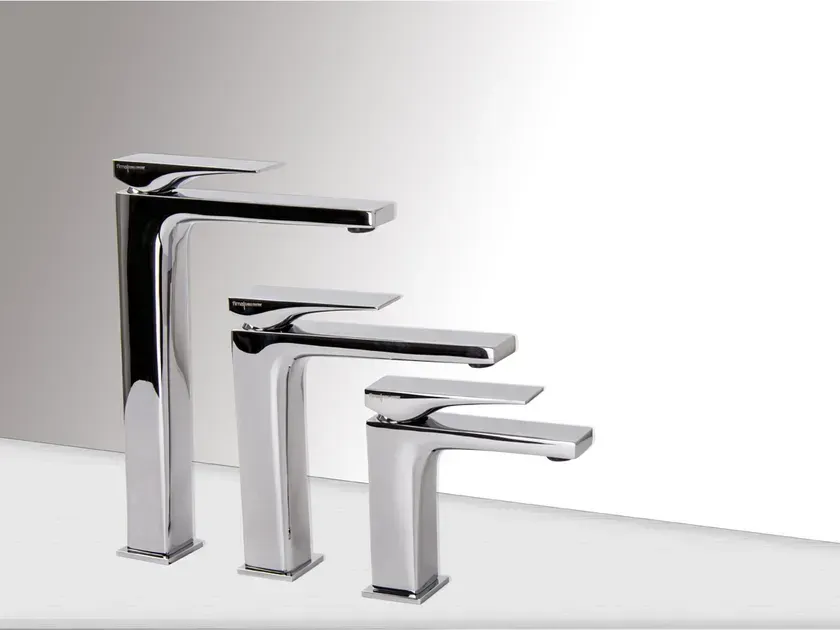 Tre rubinetti cromati di diverse altezze, disposti su una superficie bianca su uno sfondo sfumato.