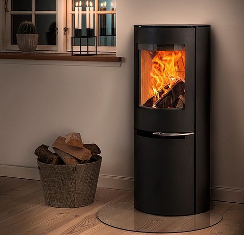 Una stufa a legna nera con il fuoco acceso all'interno, accanto a un secchio di legna e una candela accesa.