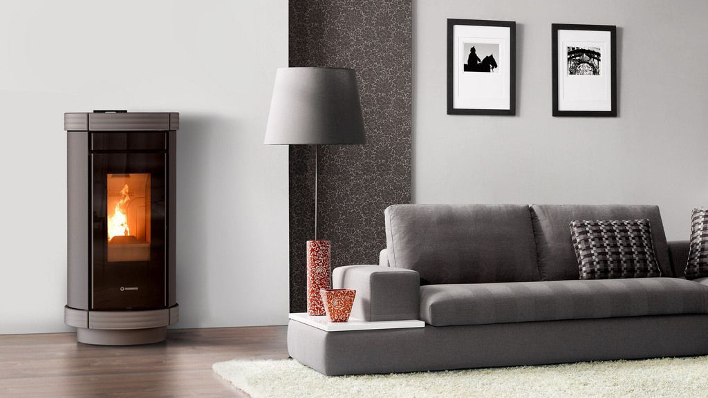 Soggiorno moderno con stufa a pellet, divano grigio e parete con quadri astratti.