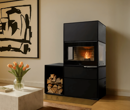 Caminetto moderno nero con sezioni rettangolari sovrapposte. Ceppi in basso a sinistra, quadri e fiori nelle vicinanze.