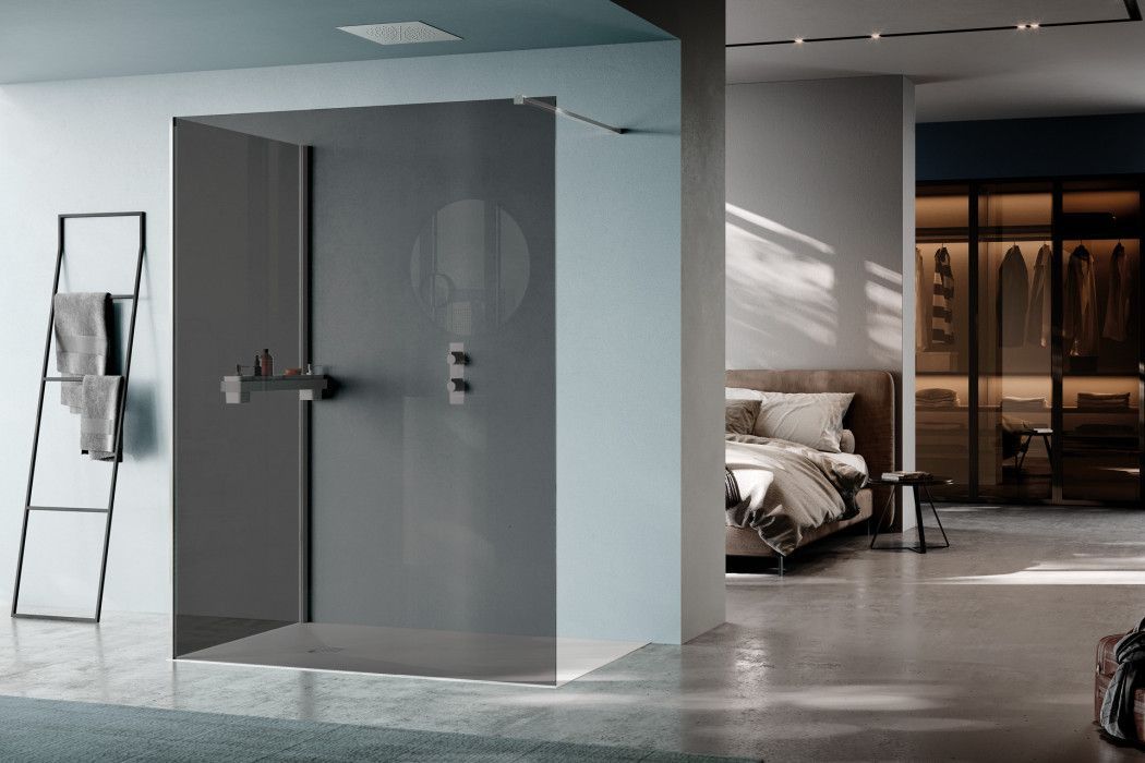 Moderna doccia aperta in una camera da letto. Pareti grigie, sanitari cromati, scala con asciugamani, letto sullo sfondo.
