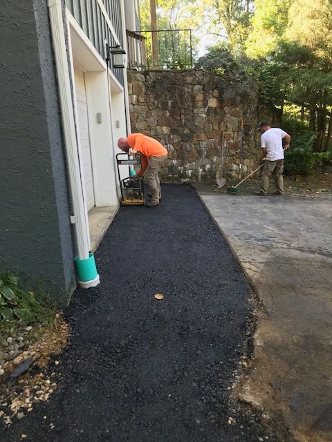 Two workers paving asphalt driveway. One compacts with a machine, the other rakes.