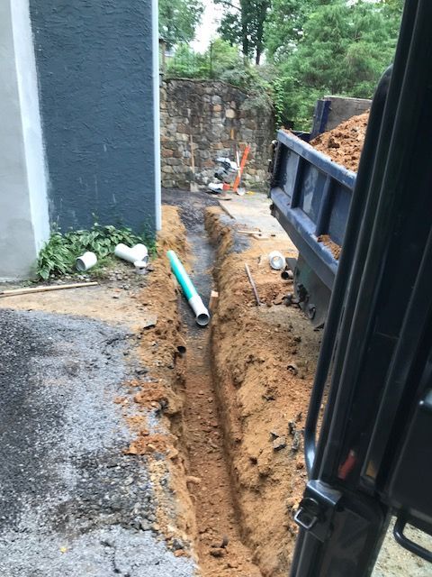 Trench dug with blue and white pipes, a dump truck, and a building under construction.