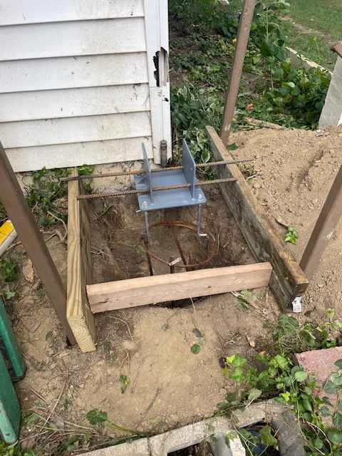 Construction site: metal bracket secured in a wooden frame, adjacent to a weathered building.