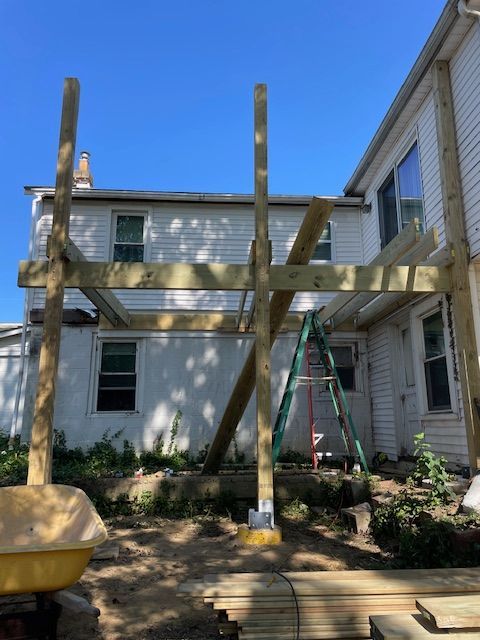 Wooden deck frame under construction next to a white house, with a ladder and tools nearby.