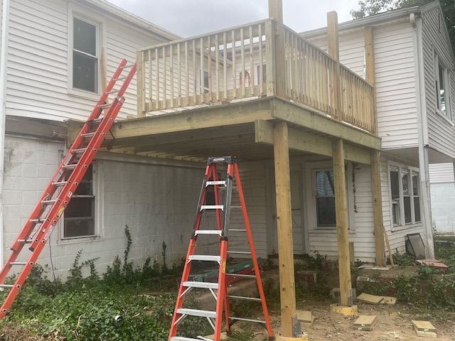 A two-story house with a newly built wooden deck. Two ladders lean against the house.