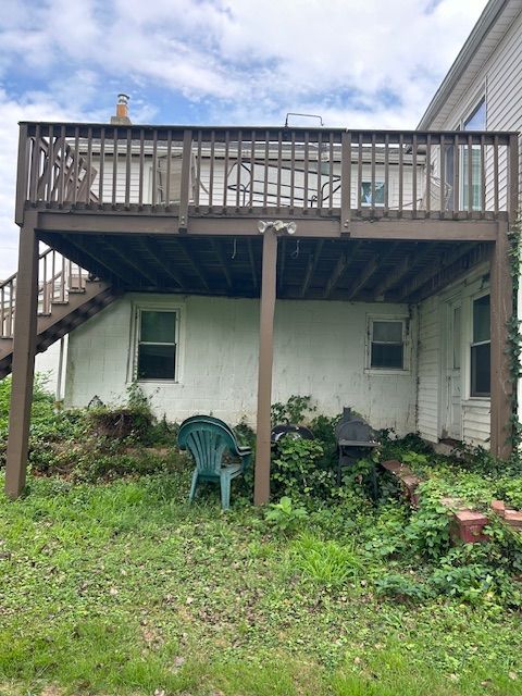 Backyard with a two-story wooden deck attached to a white building; overgrown grass and greenery in front.