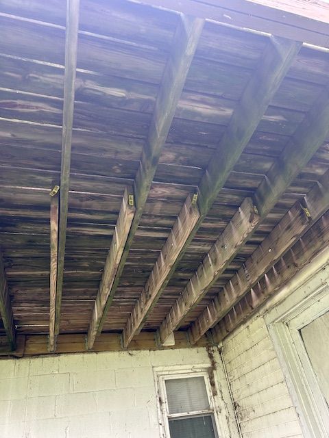 Overhead view of weathered wooden porch ceiling with beams and boards. Light shines down.