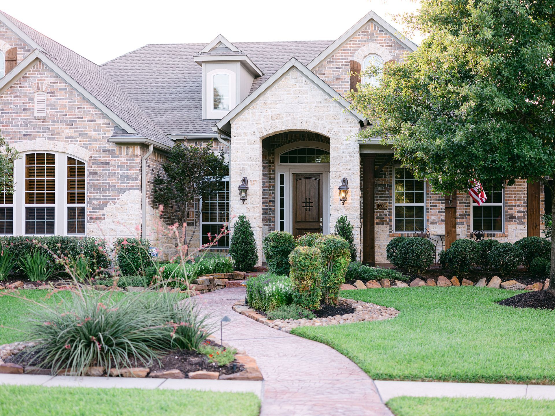 A large brick house with a lush green lawn and a walkway leading to the front door.