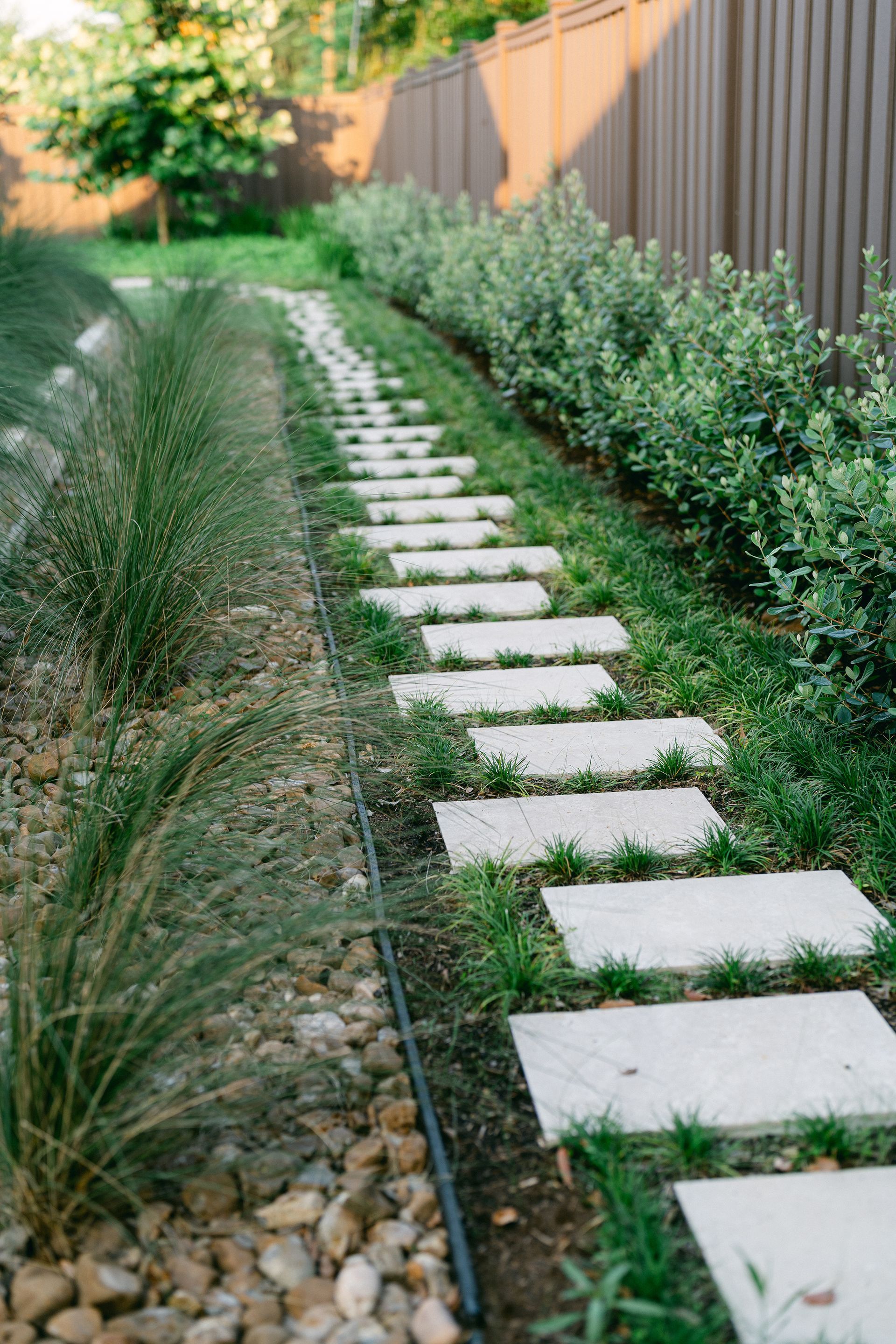 A stone walkway leading to a fence in a backyard.