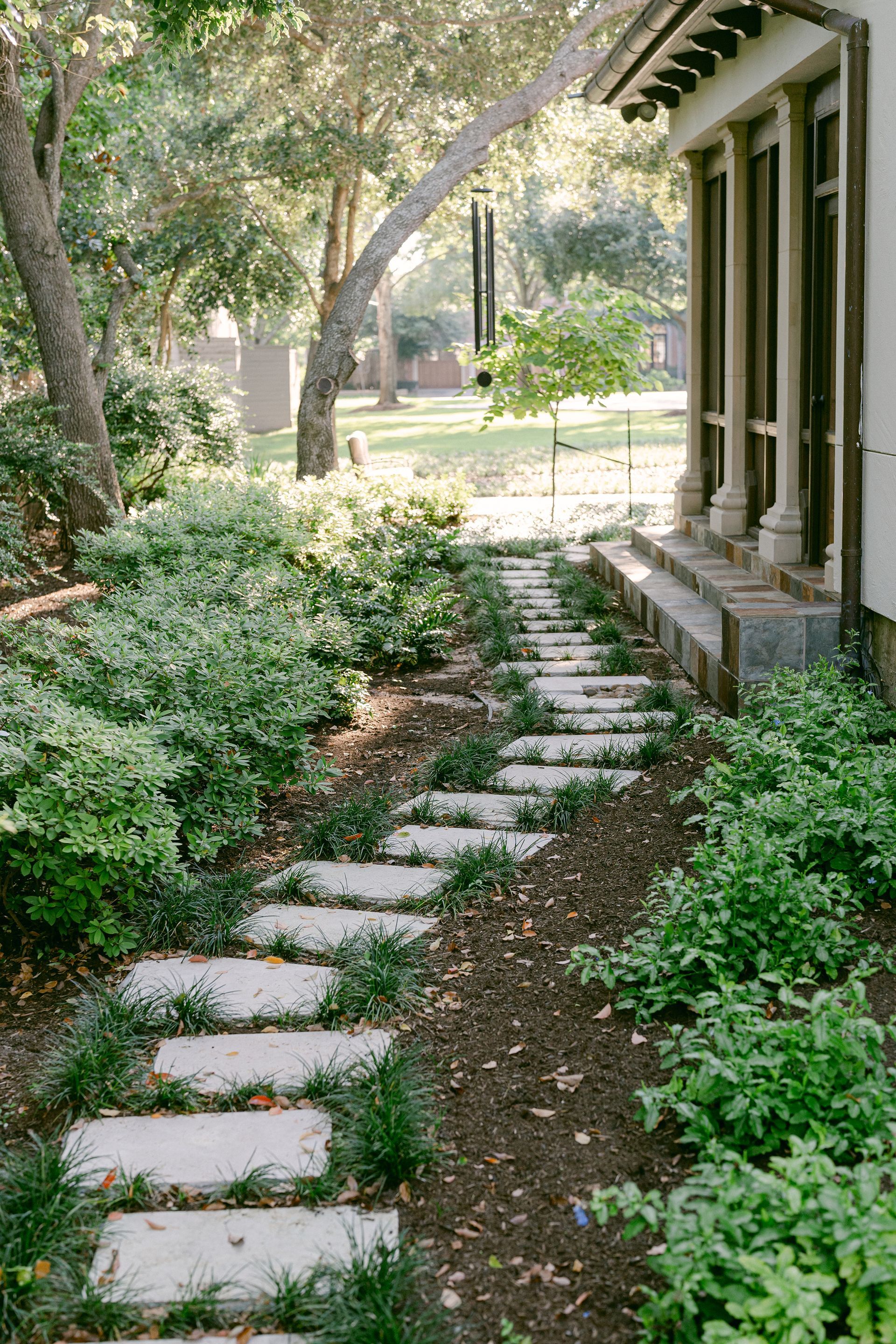 A stone walkway leading to a house in a garden.