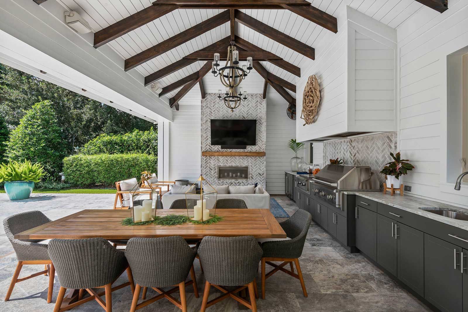 There is a table and chairs in the middle of an outdoor covered patio with outdoor kitchen