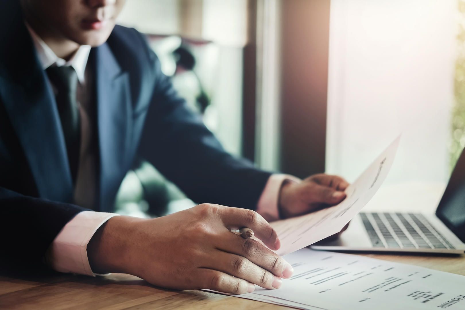 A man in a suit and tie is sitting at a desk looking at a piece of paper.