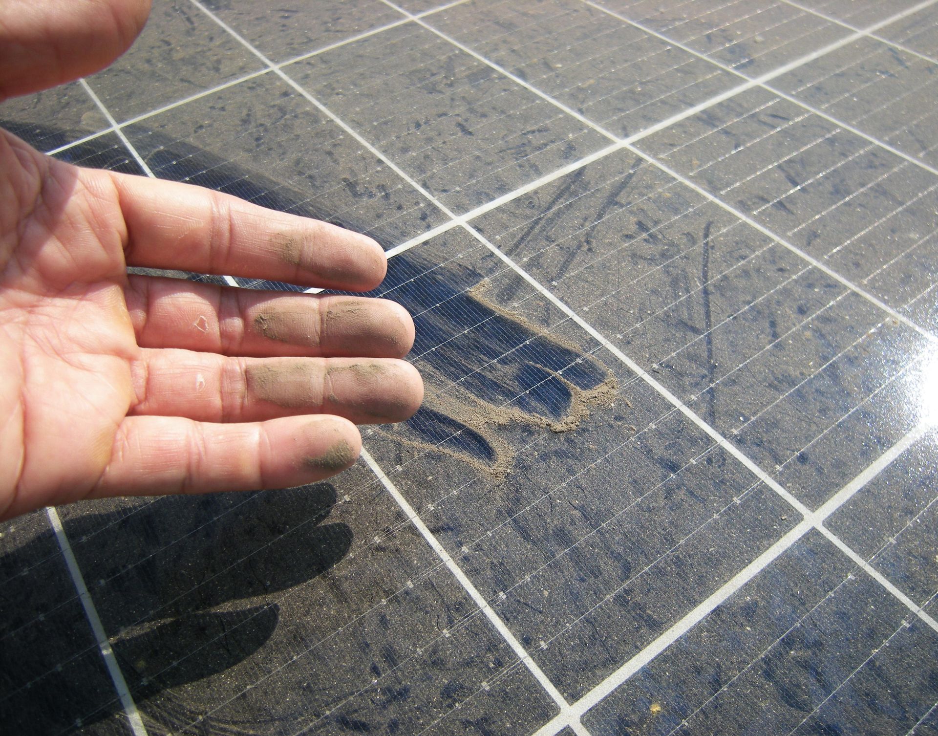 Hand resting over a dark tiled floor with sunlight and a small puddle of water or stain