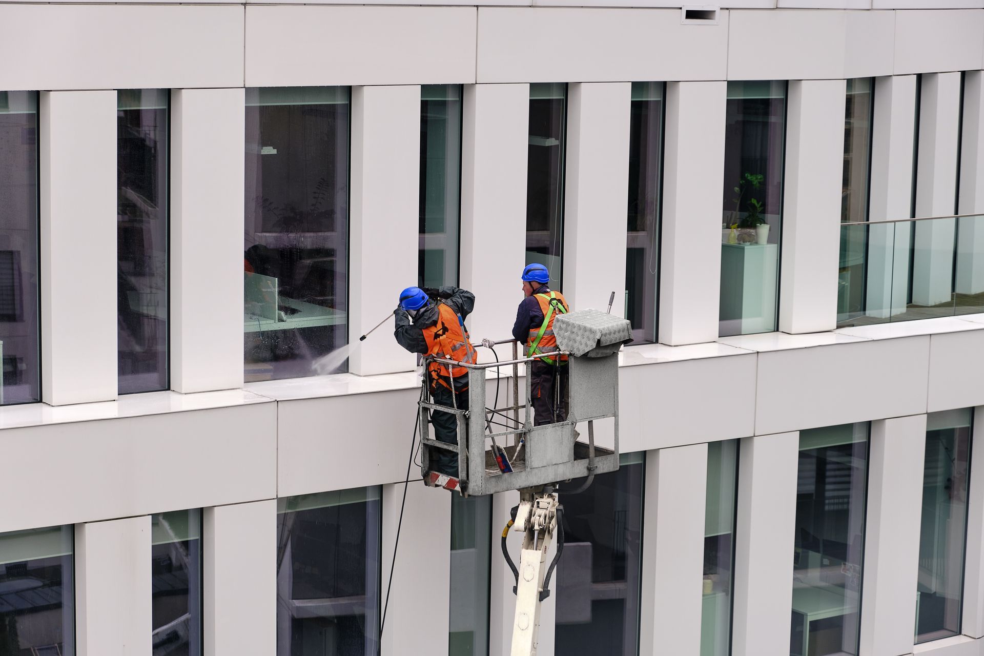 Two window washers on a suspended platform cleaning a white high-rise building exterior