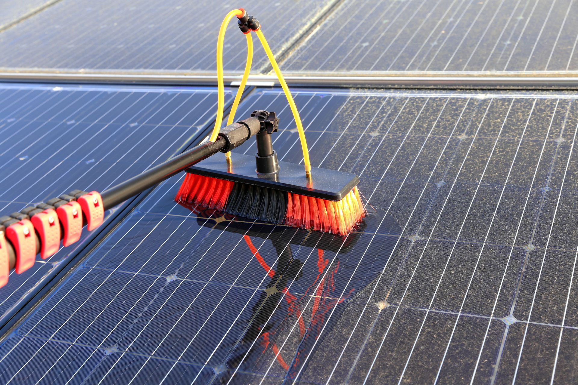 Roof cleaner using a long-handled brush to wash solar panels on a rooftop