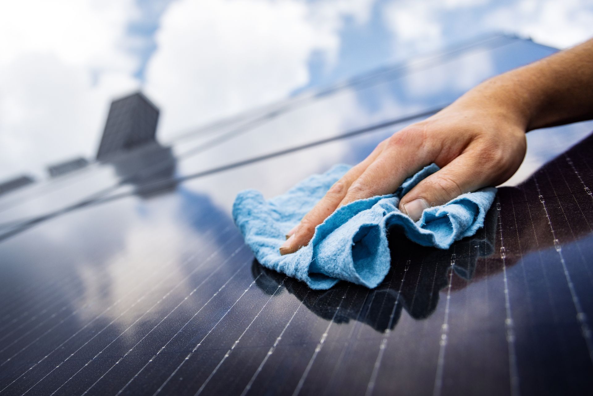 Hand wiping a solar panel with a blue cloth outdoors