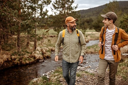 A man and a boy are walking along a river.