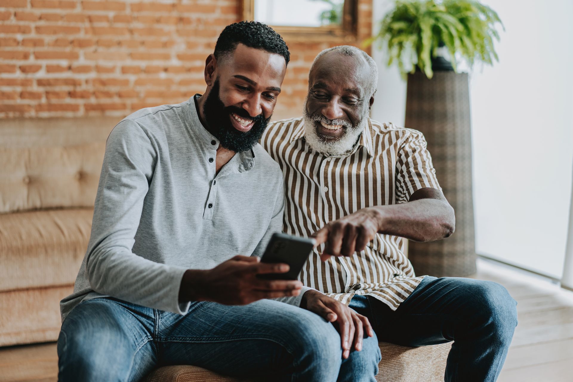 Two men are sitting on a couch looking at a cell phone.