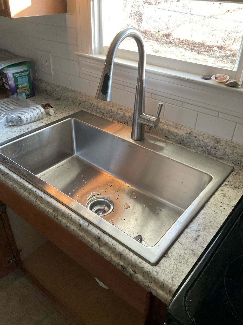 A stainless steel kitchen sink with a faucet on a granite counter top.